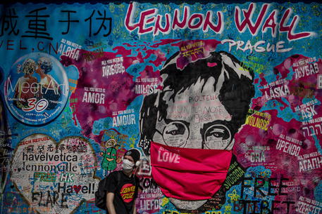 Un uomo passa davanti ad un murales dedicato a John Lennon con naso e bocca coperti a Praga © EPA