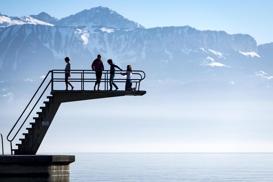 Un gruppo di ragazzi si gode la bella giornata su un trampolino sopra il lago di Ginevra di fronte alle Alpi © Ansa